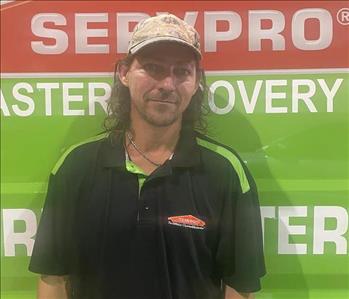 Male with long hair in baseball cap and black SERVPRO shirt standing in front of SERVPRO vehicle 