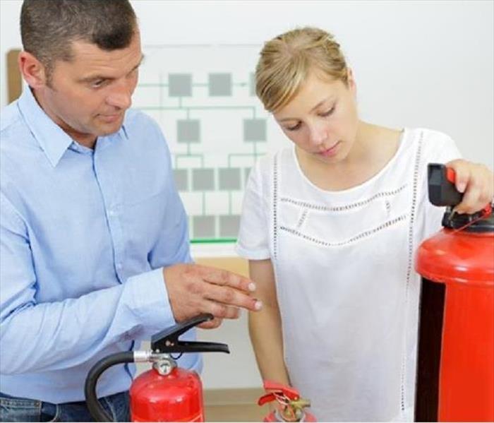 two people in a meeting room looking at multiple fire extinguishers