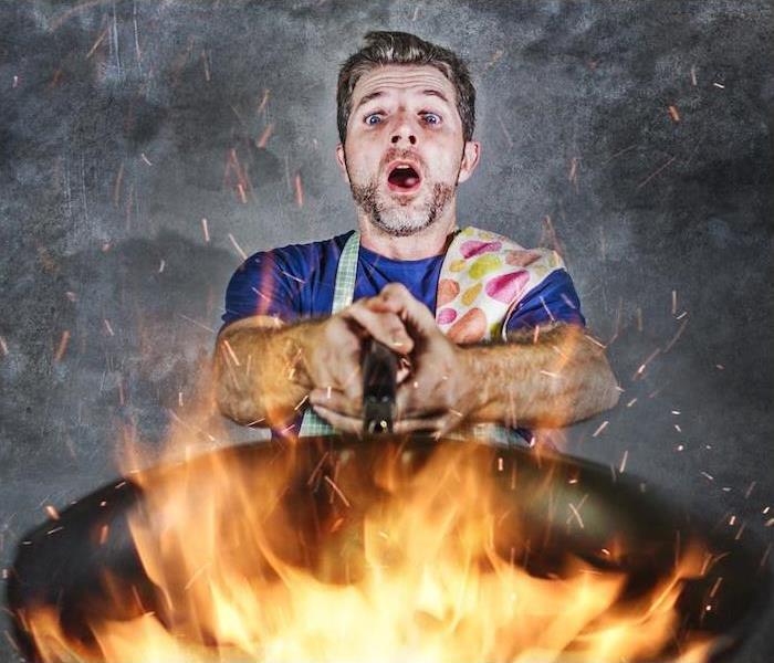 a person with a blue shirt wearing a apron holding a pan with flames flaring up out of it